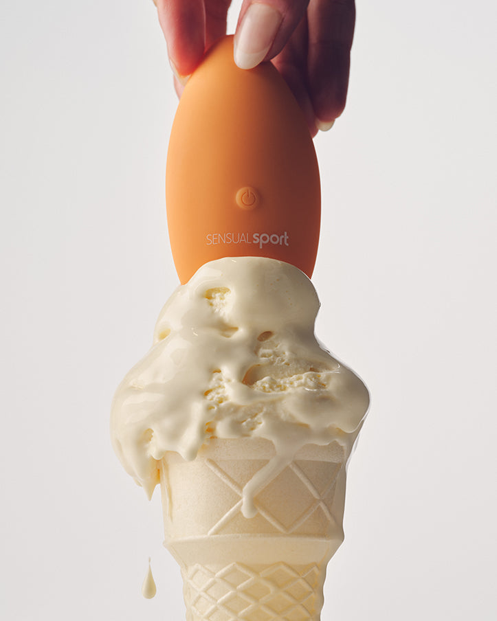 A hand holds an orange "SENSUAL sport" device above a melting vanilla ice cream cone, with drips running down the sides against a clean, white background.