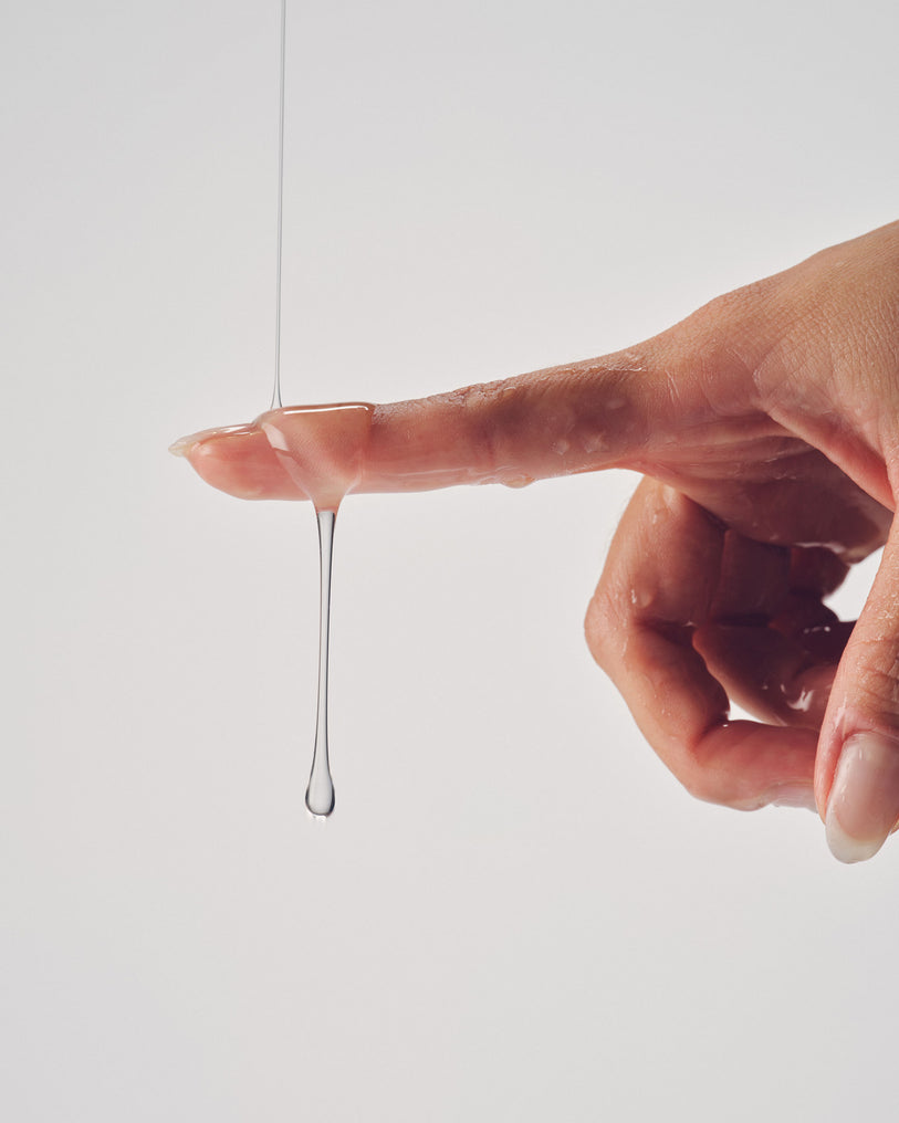 A hand with a translucent liquid dripping from a fingertip, creating a sensual and intimate effect.